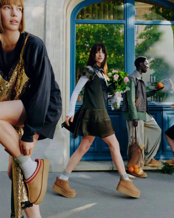 Two women walking on a street, wearing brown shoes.